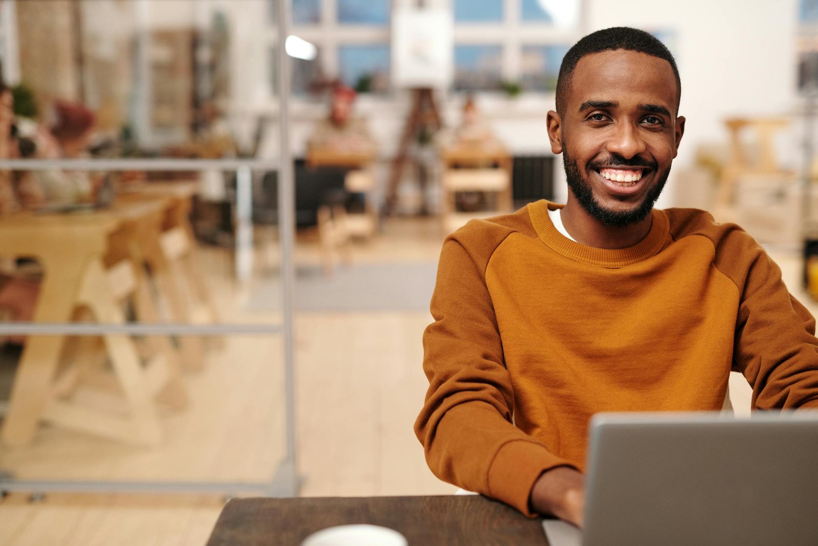 Confident man in brown sweater working on laptop in cozy office.